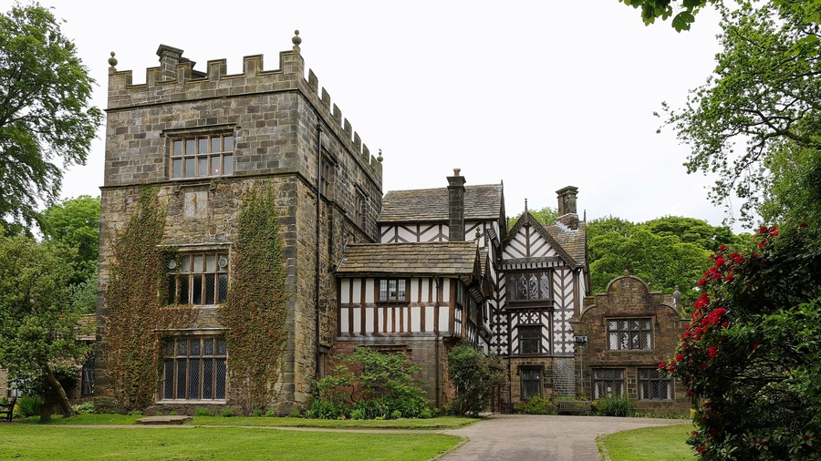 A large stone building with a tower and a Tudor-style house.