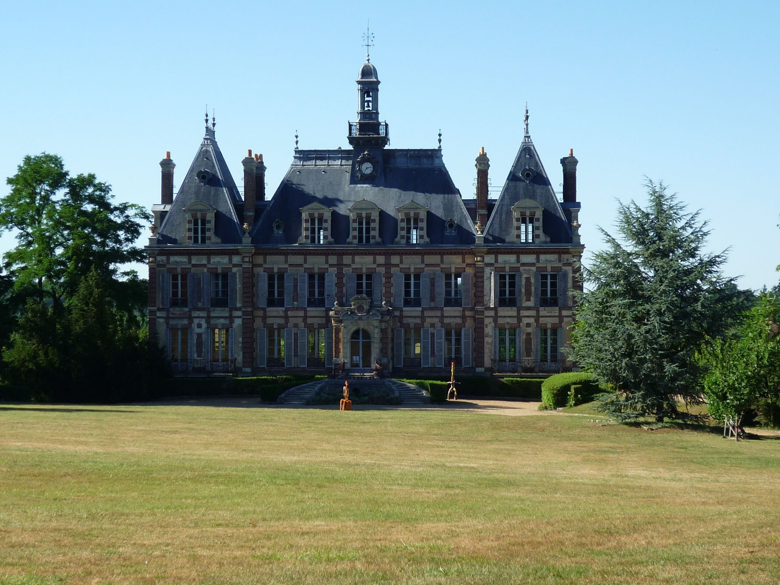 A large, historic building with a clock tower, surrounded by a well-maintained lawn and trees.