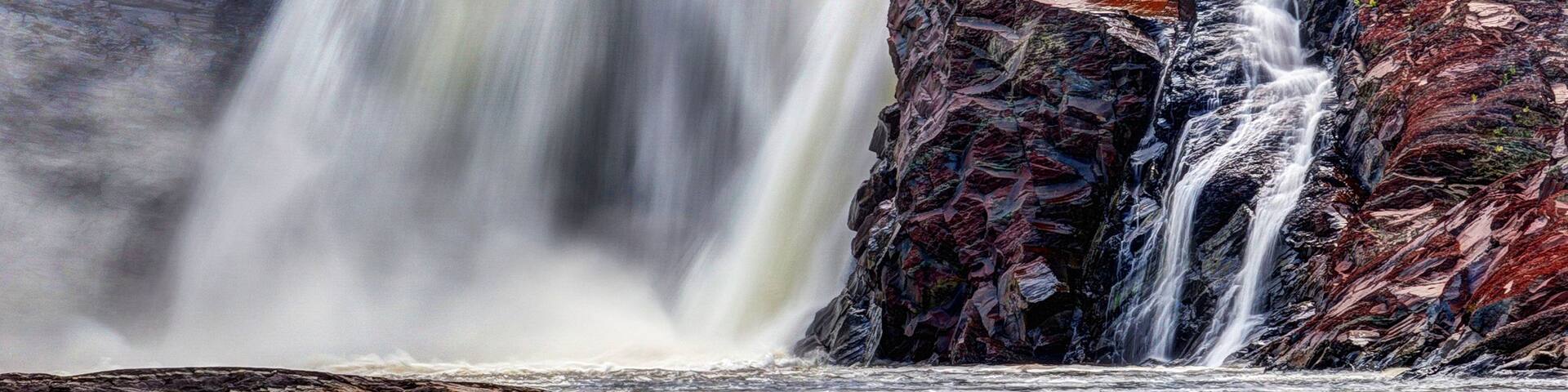 A powerful waterfall cascading over multicolored rocks into a calm river.