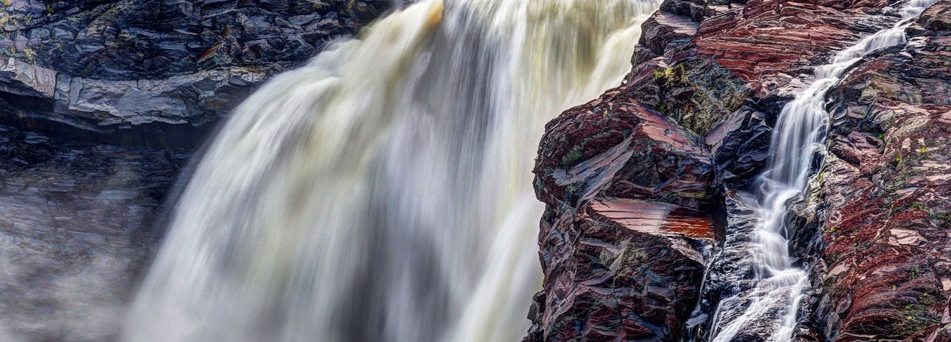 Uma cachoeira imponente despencando sobre rochas multicoloridas em um rio calmo.
