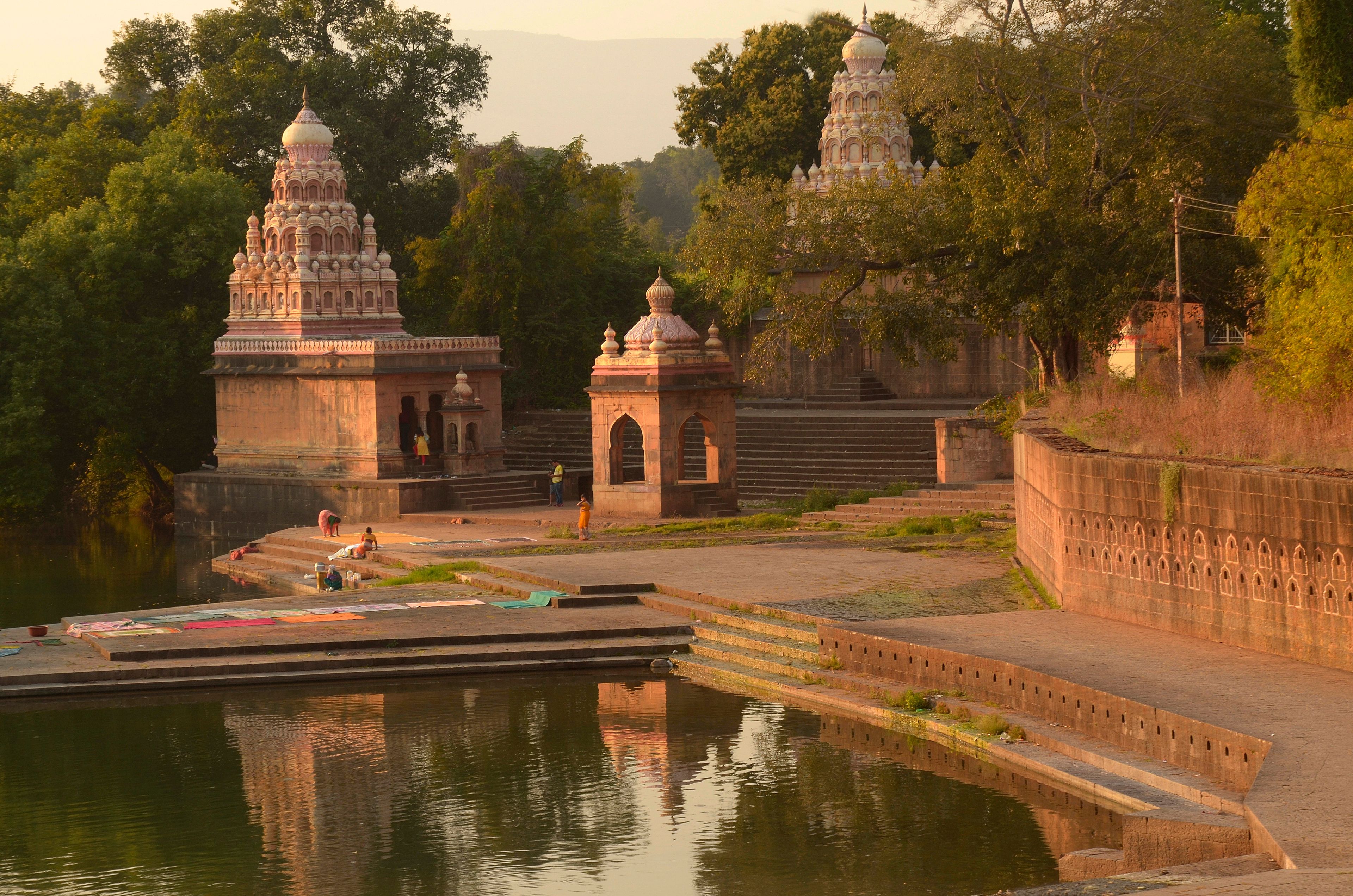 A temple complex with two main structures, a water body in the foreground, and a stone wall with arched openings.