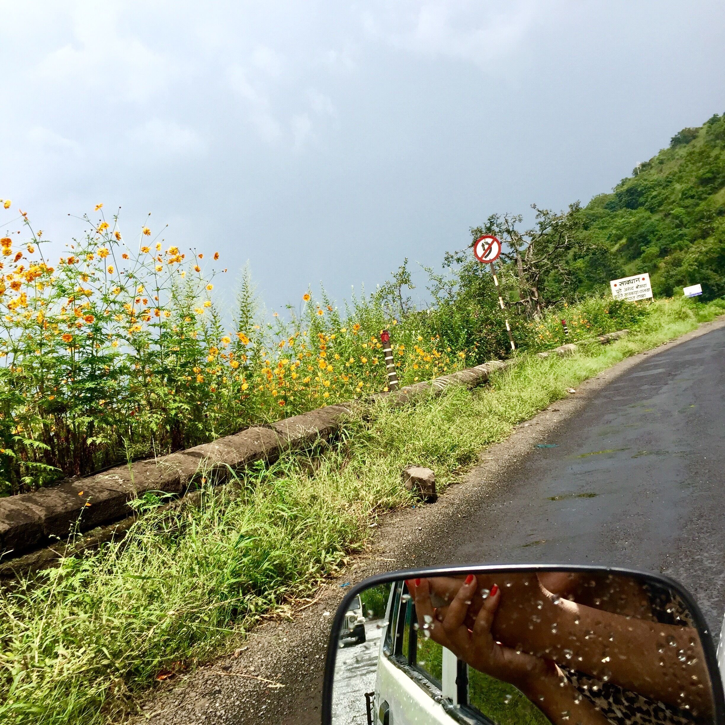 A rural road with a no U-turn sign, a guardrail, and a signboard in a hilly area.