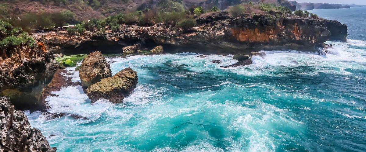 A coastal landscape with rocky cliffs, turquoise waters, and green vegetation.