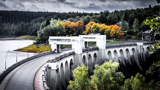 A dam with a bridge, a river, and autumn foliage.