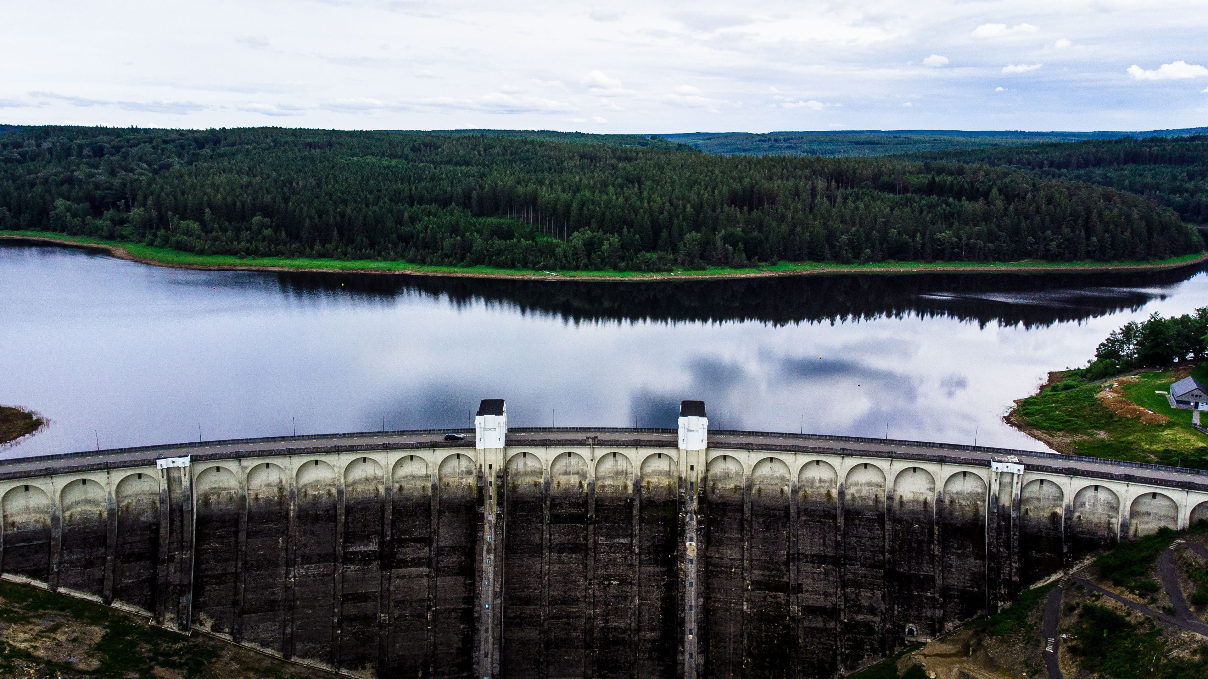 A dam with multiple arches, a calm lake, and a forested landscape in the background.