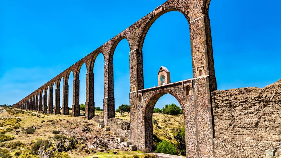 A long stone viaduct with multiple arches, a small tower, and a hilly landscape.