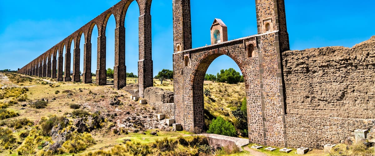 A long stone viaduct with multiple arches, a small tower, and a hilly landscape.