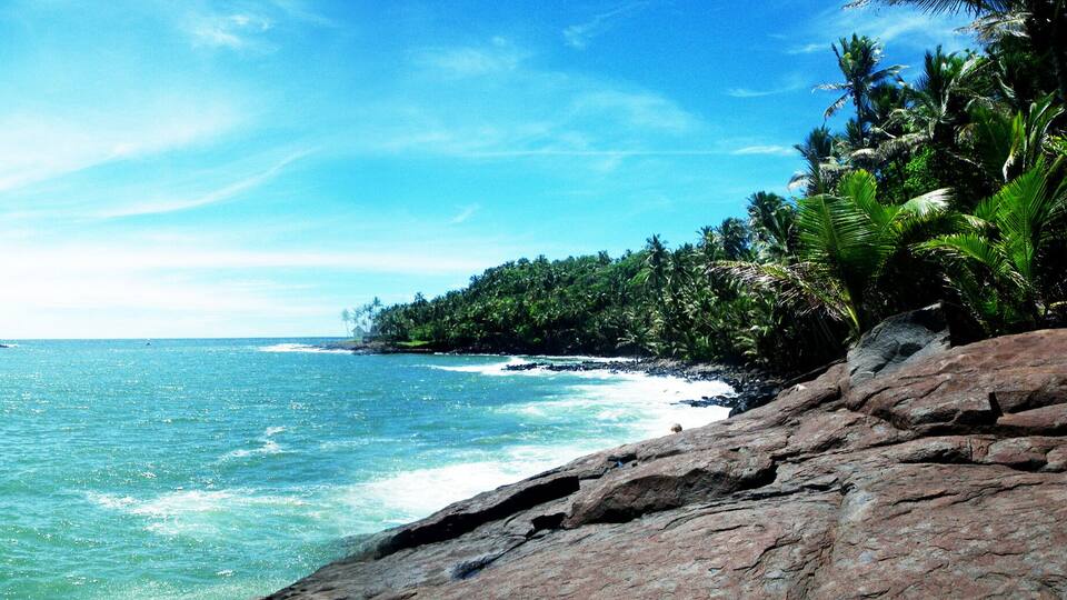 A tropical beach with clear turquoise waters, a rocky shoreline, and a small island in the distance.