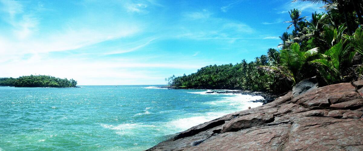 A tropical beach with clear turquoise waters, a rocky shoreline, and a small island in the distance.