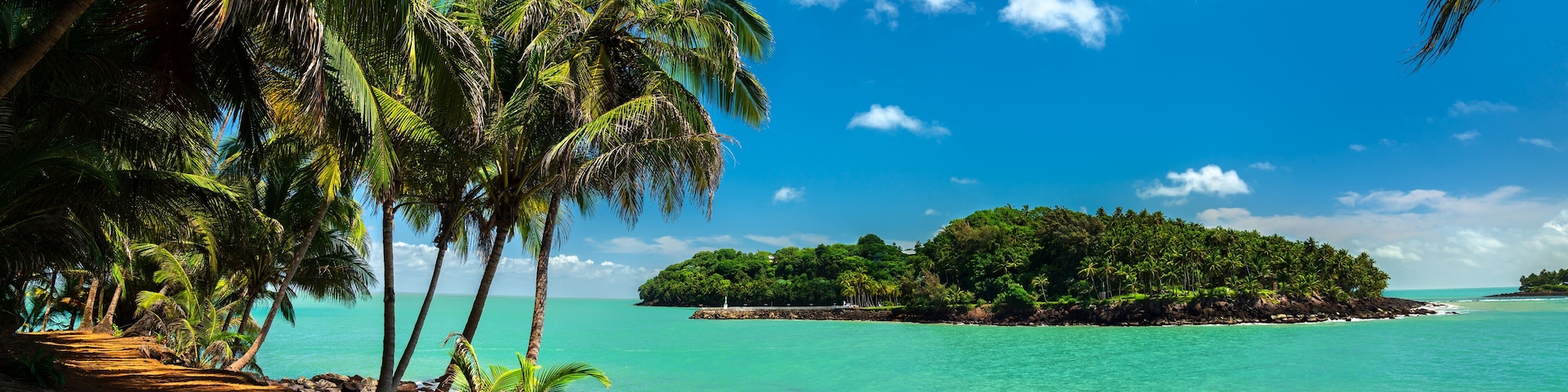 Uma praia tropical com palmeiras, águas turquesa cristalinas e uma pequena ilha ao longe.