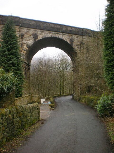 Uma estrada estreita sob uma ponte de pedra, ladeada por árvores.