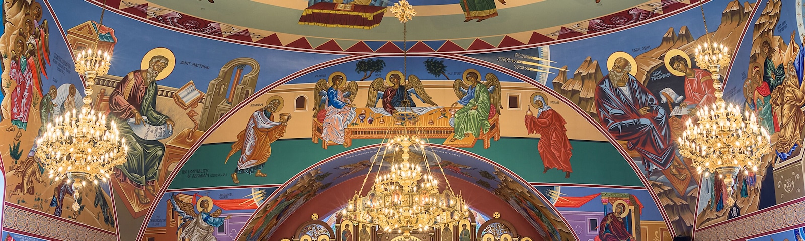 Interior de igreja ornamentado com um grande candelabro, pinturas religiosas e fileiras de bancos.