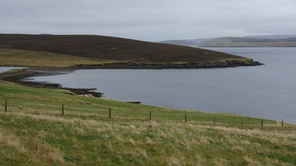 A coastal landscape with a grassy hill, a body of water, and a distant shoreline.