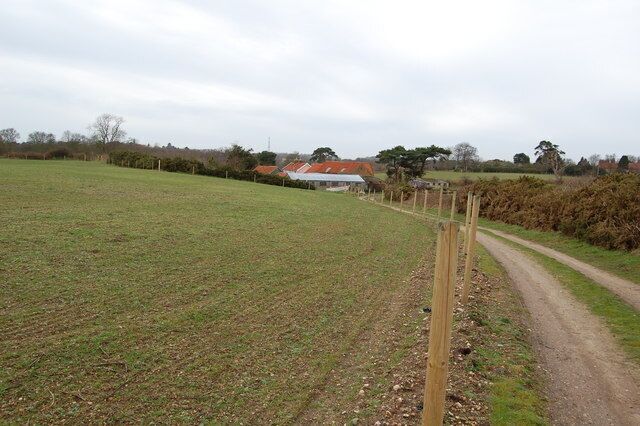 A rural landscape with a dirt road, a wooden fence, and a house with a red roof.