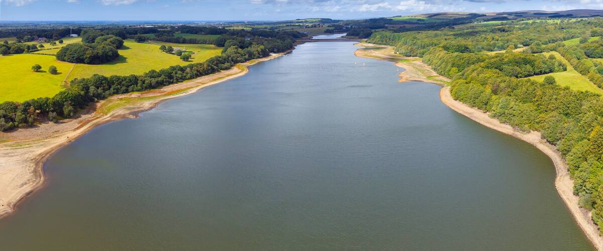Un río serpentea por un paisaje verde con campos y árboles, bajo un cielo parcialmente nublado.