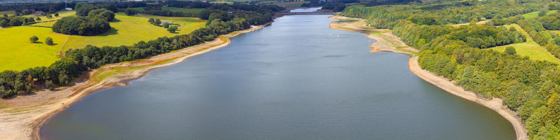 A river meandering through a green landscape with fields and trees, under a partly cloudy sky.