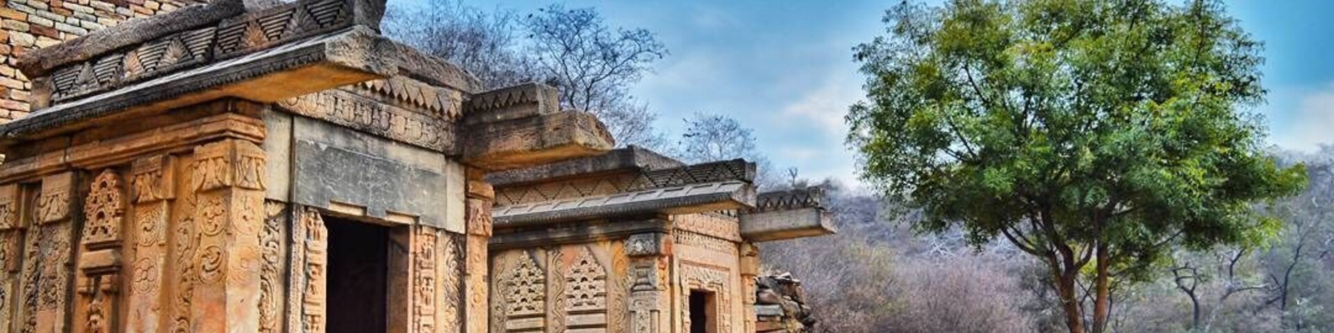 Una estructura de piedra antigua con tallados intrincados, un árbol y un sendero de piedra.