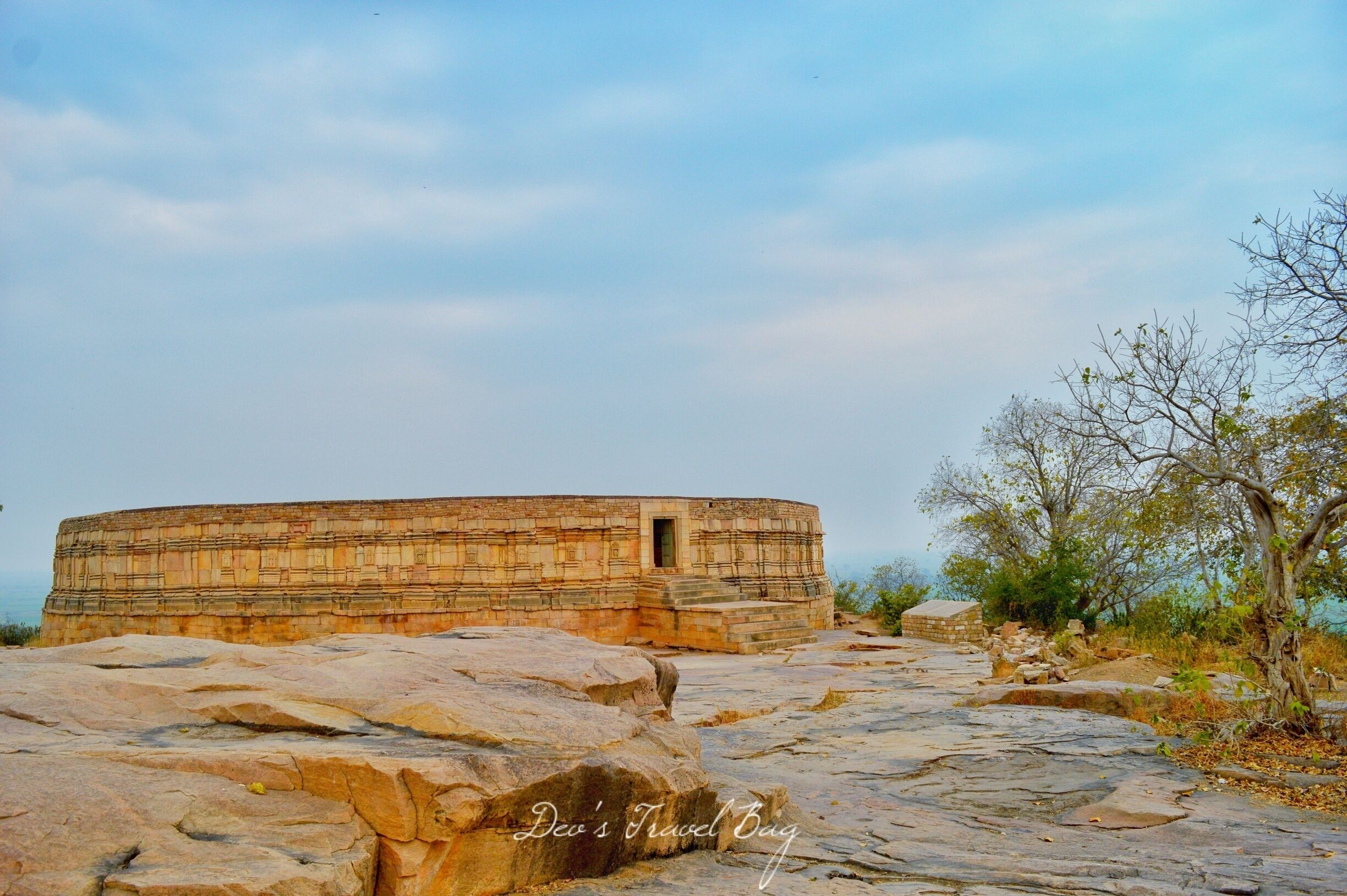 A large, ancient stone structure with a small doorway, surrounded by rocky terrain and sparse vegetation.