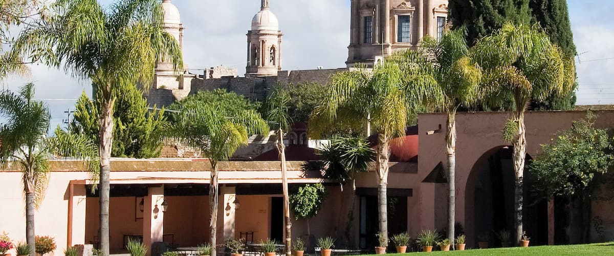 A large domed building with two smaller domes, surrounded by palm trees and a paved courtyard.