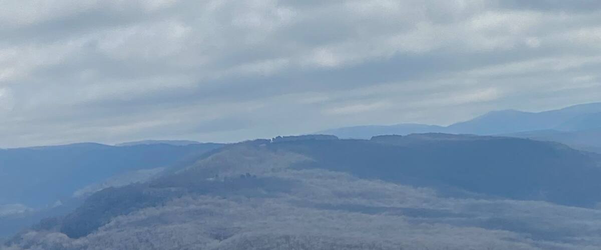 A mountainous landscape with rolling hills and a clear sky with scattered clouds.