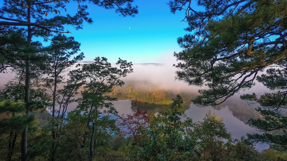 A forested landscape with a lake reflecting trees and a clear sky.