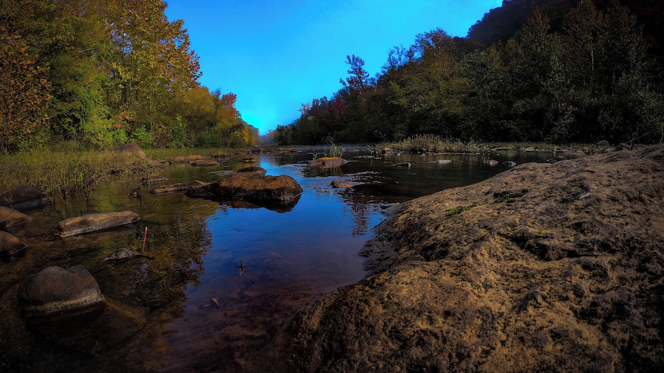 A river with clear water, surrounded by rocks and trees.