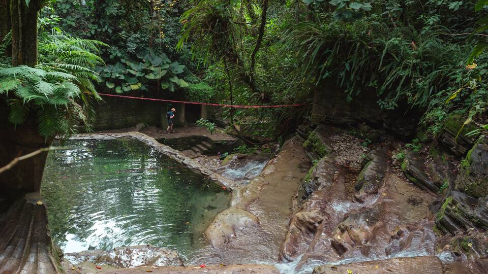 A natural water feature with a person standing on a rock ledge.