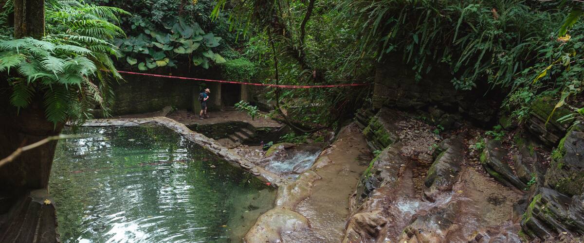 A natural water feature with a person standing on a rock ledge.