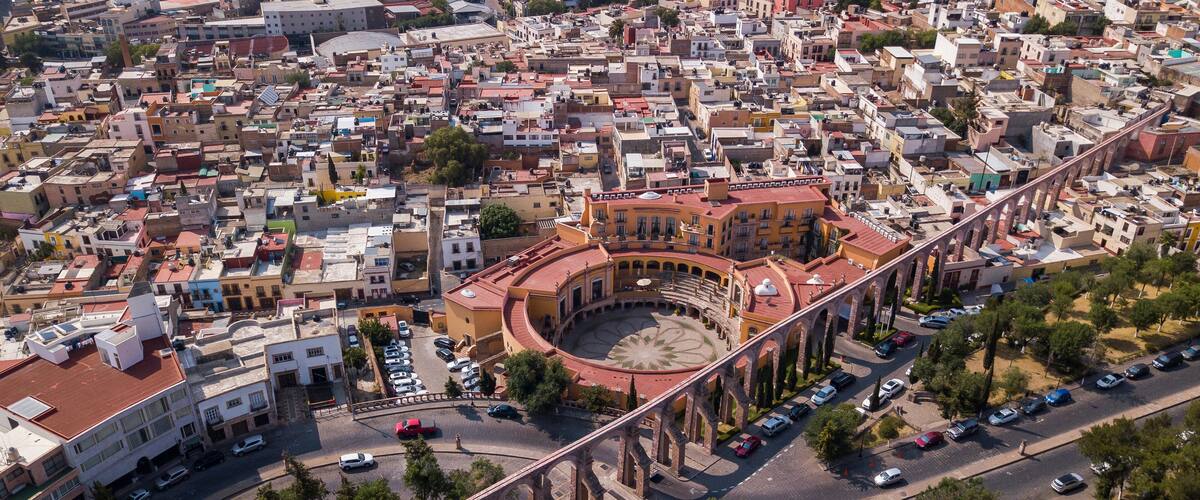 An aerial view of a city with a prominent circular building surrounded by a bridge.
