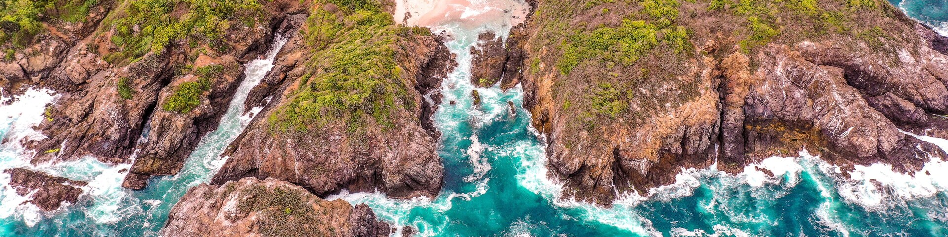 A coastal landscape with rocky cliffs, turquoise waters, and a sandy beach.