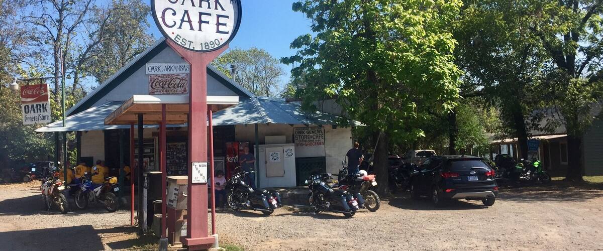 A historic general store and cafe with a sign, motorcycles parked outside, and a Coca-Cola sign in the background.