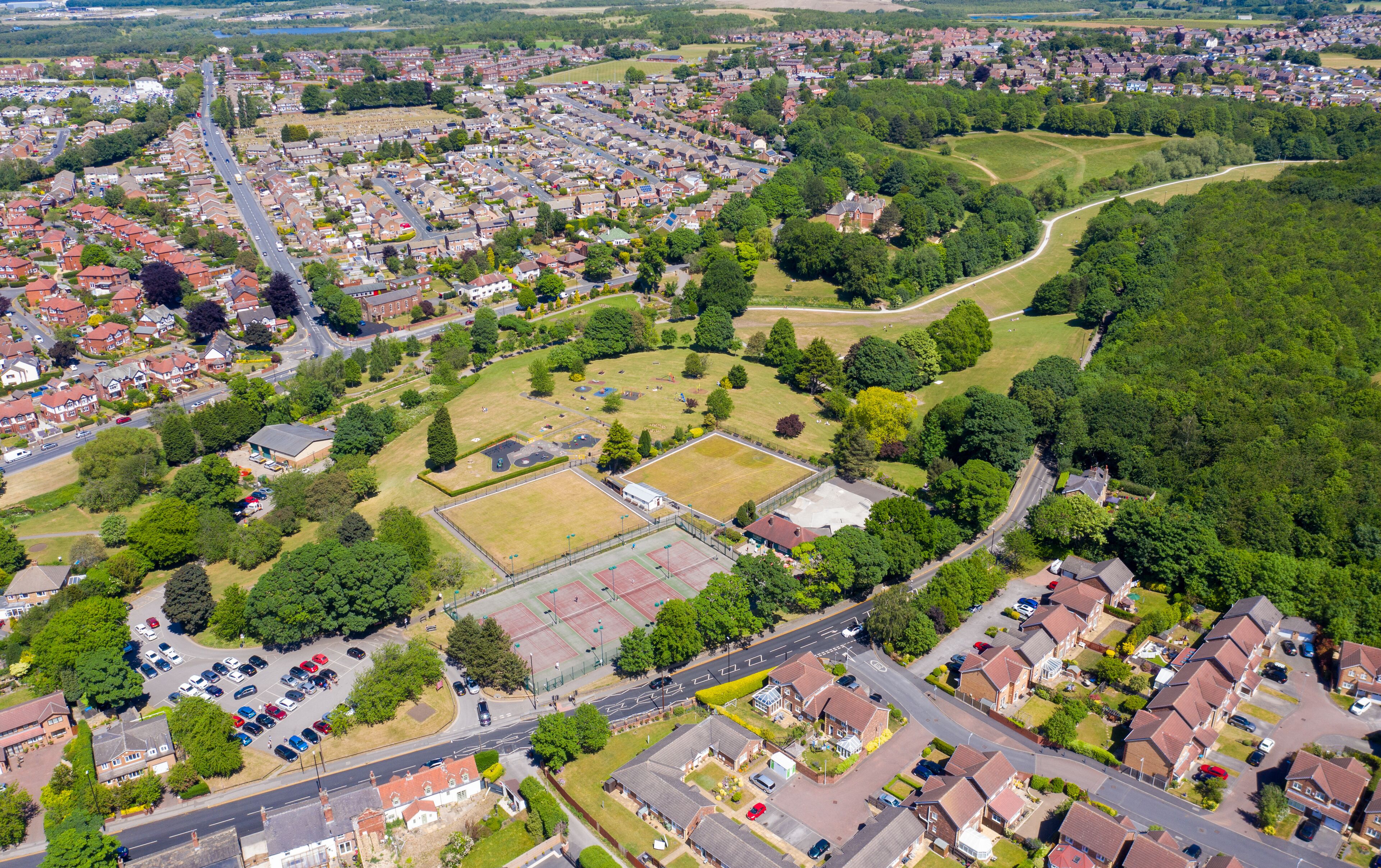 An aerial view of a residential area with houses, roads, and a large green park.