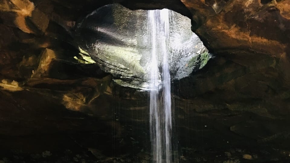 A waterfall in a cave with rocky terrain.