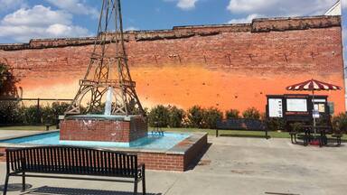 A water fountain, a brick wall, and a bench in a park.