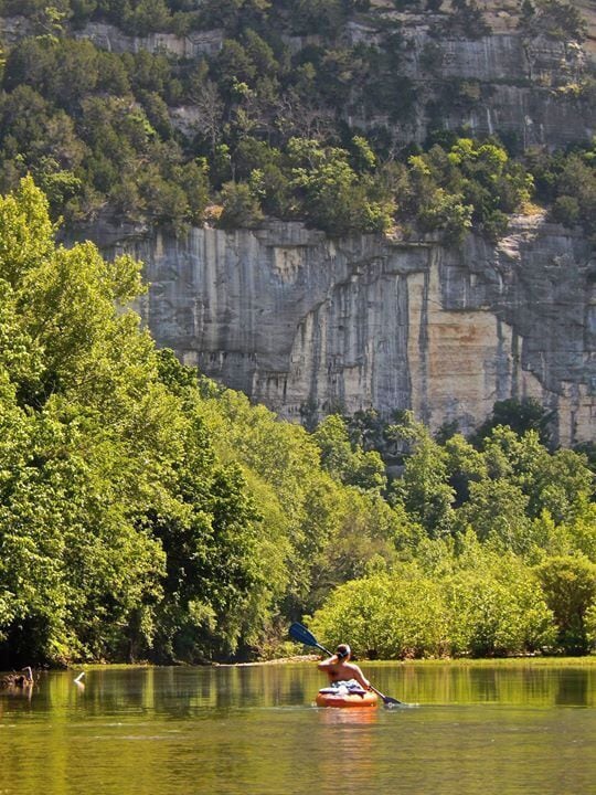 A kayaker on a river surrounded by cliffs and dense greenery.