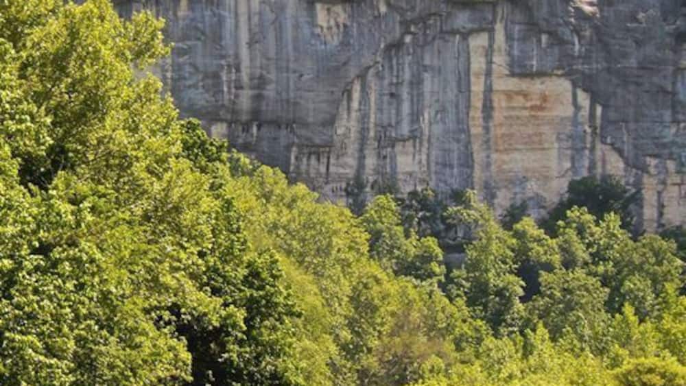 Un kayakiste navigue sur une rivière bordée de falaises et d’une végétation luxuriante.