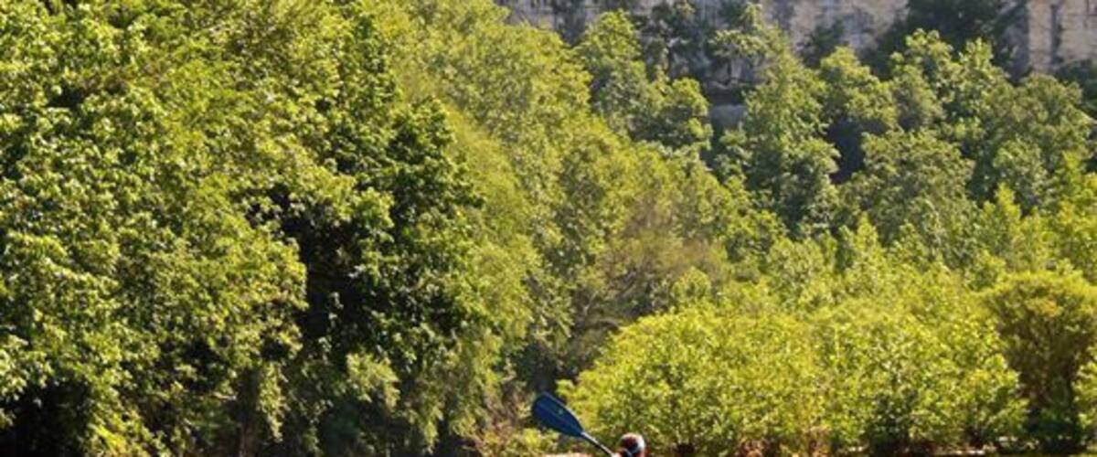A kayaker on a river surrounded by cliffs and dense greenery.