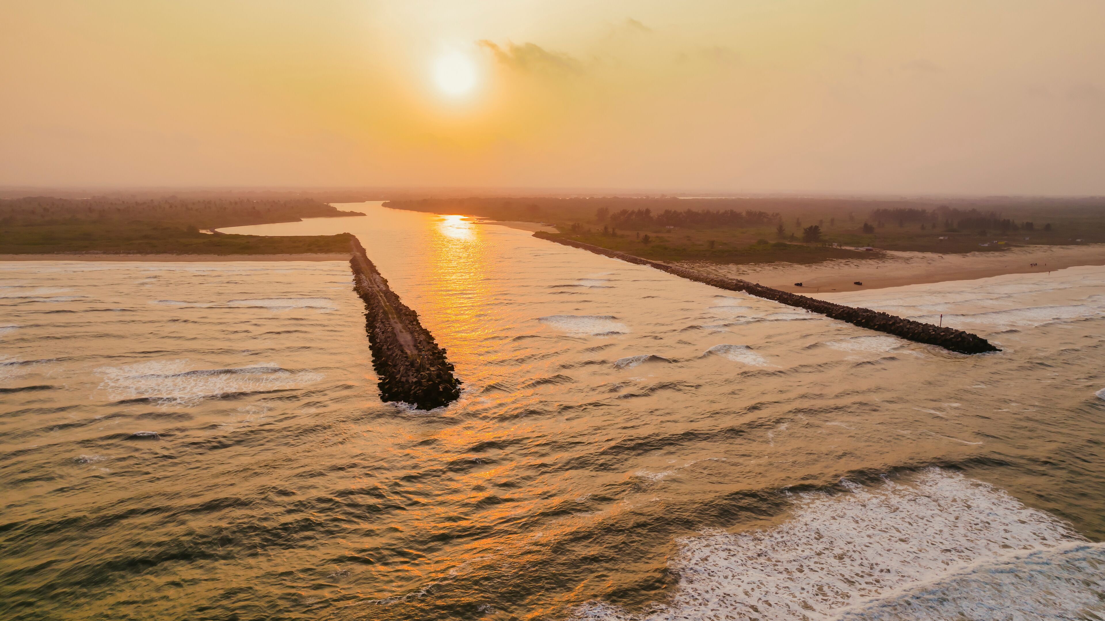 A river with a long, narrow island in the middle, surrounded by fields and a sunset in the background.