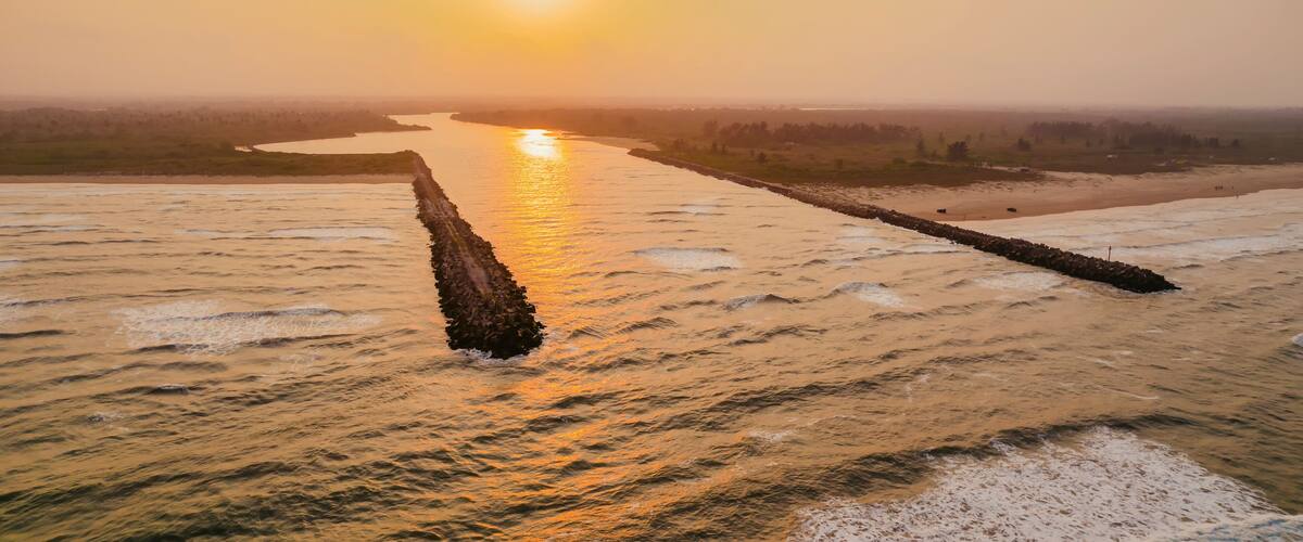 A river with a long, narrow island in the middle, surrounded by fields and a sunset in the background.