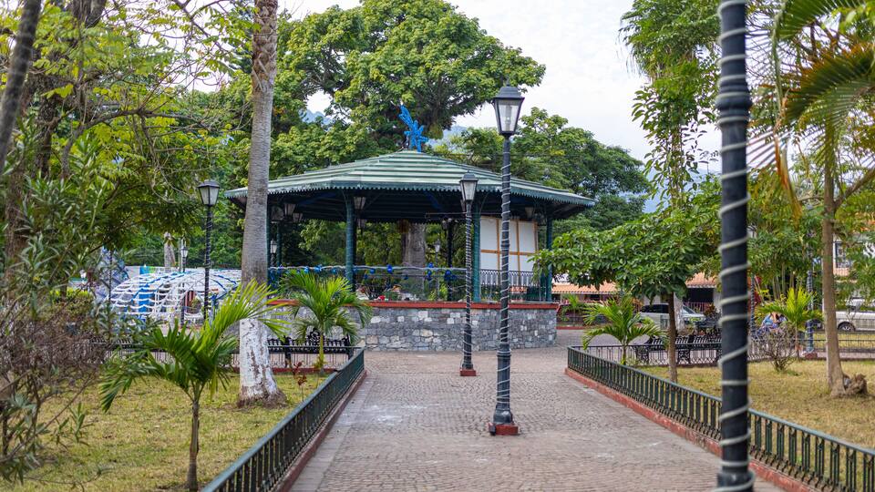 A gazebo with a green roof and blue accents, surrounded by trees and a cobblestone path.