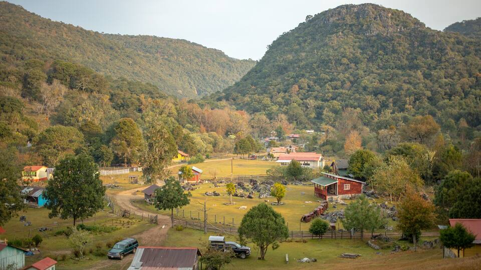 A rural landscape with rolling hills, a fenced pasture, and scattered buildings.