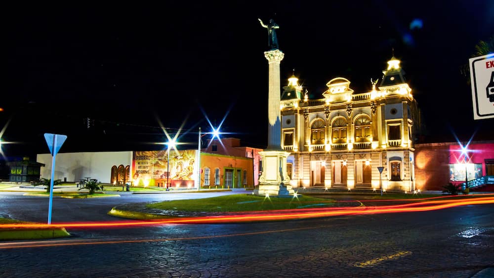 view of street at night with building illuminated, and lights of car in foreground, hidalgo theather in parral chihuahua