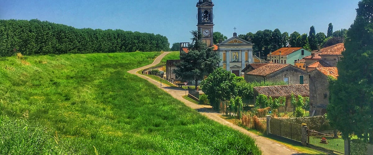 A village with a prominent church tower, lush green fields, and traditional buildings.