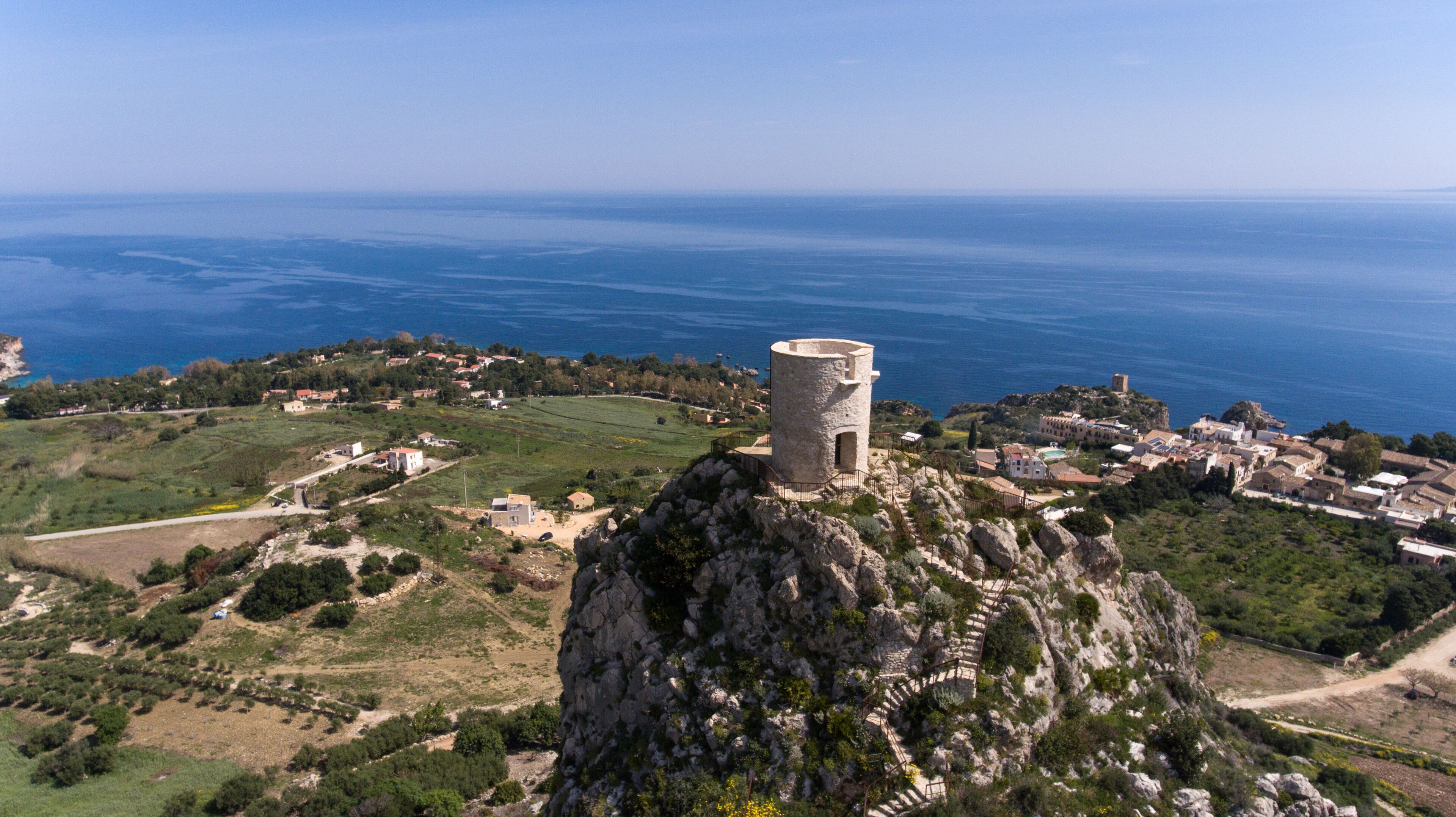 A coastal village with a prominent tower on a rocky outcrop, surrounded by fields and the sea.