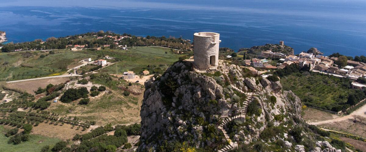 A coastal village with a prominent tower on a rocky outcrop, surrounded by fields and the sea.