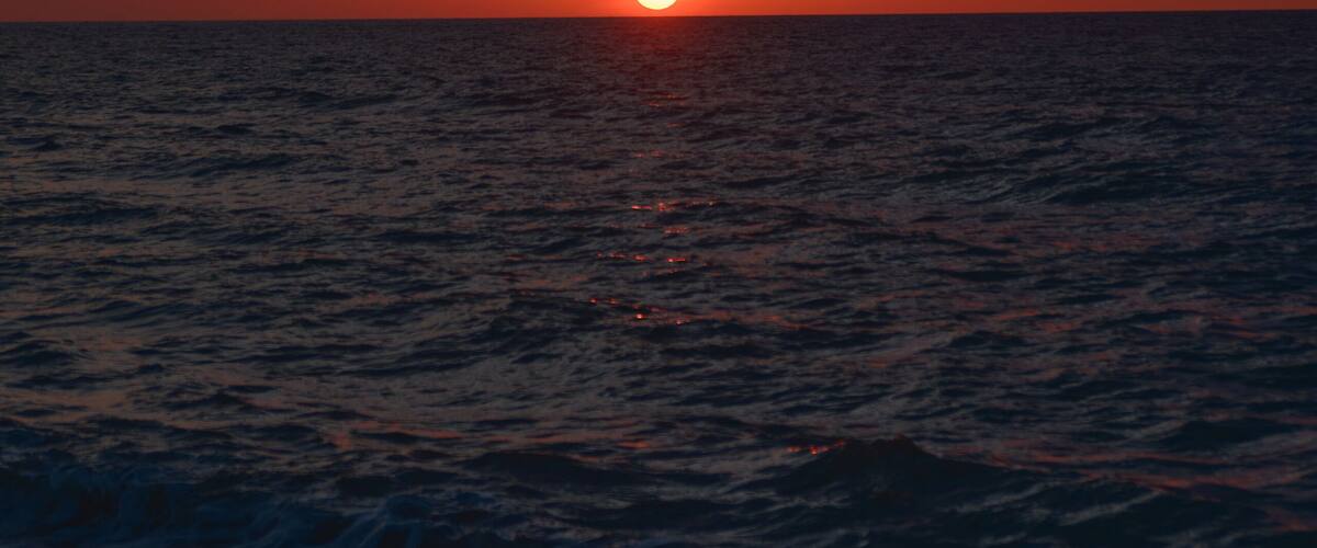 A sunset over the ocean with the sun near the horizon and clouds in the sky.