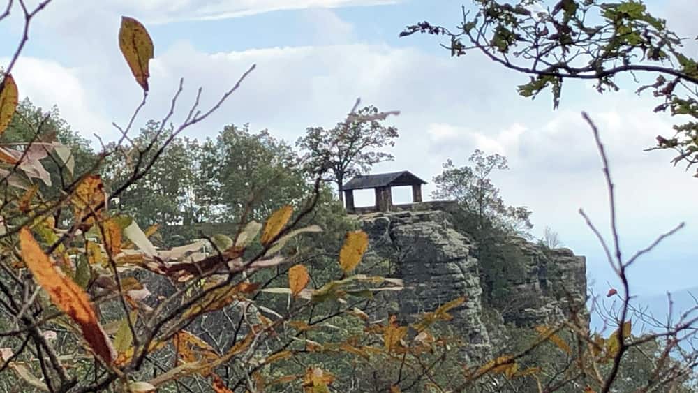 A rocky outcrop with a small wooden structure on top, surrounded by autumn foliage.