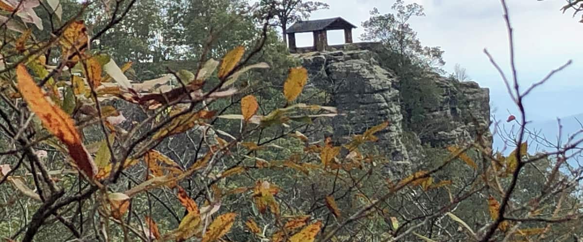A rocky outcrop with a small wooden structure on top, surrounded by autumn foliage.