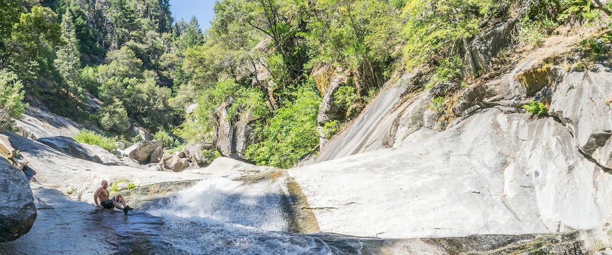 A waterfall cascading over rocks into a pool of water, surrounded by lush greenery.