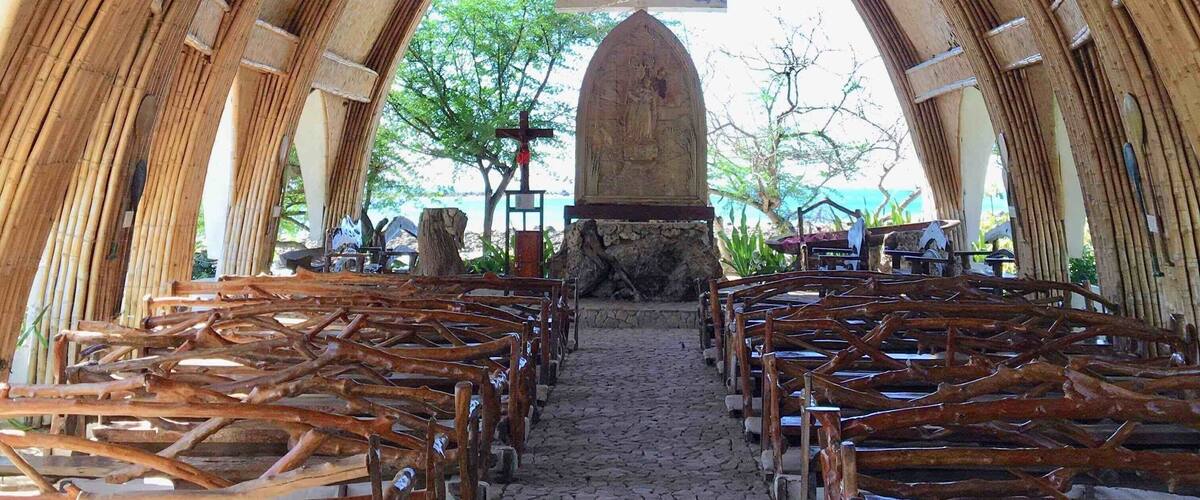 A church interior with a stone altar, wooden pews, and a cross.